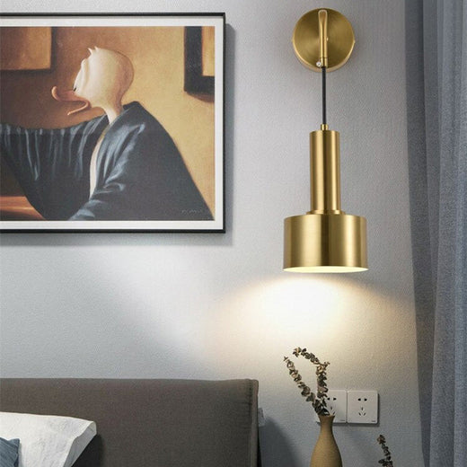 Applique murale dorée style industriel suspendu, diffusant une lumière chaude sur le mur.