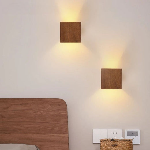 Deux appliques murales bois cubiques LED diffusent une lumière chaude vers le haut et le bas.