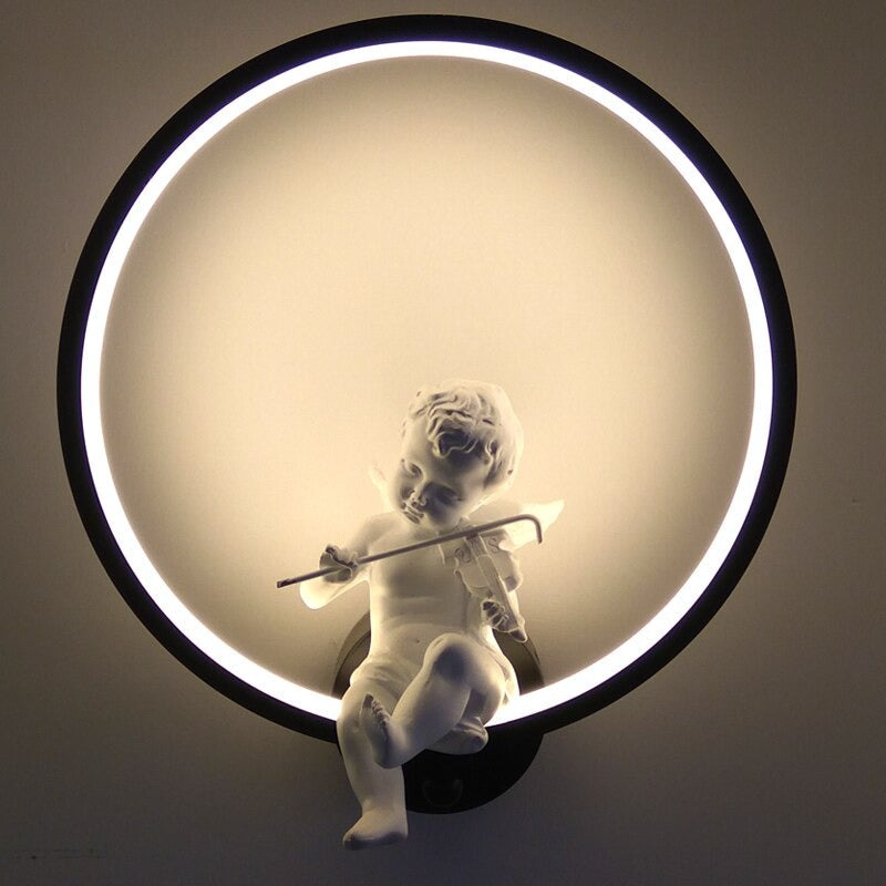 La Maison Applique "Applique murale cuisine design ange" présente un halo LED unique avec un chérubin blanc jouant de la flûte, diffusant une lumière douce et décorative et ajoutant de l'élégance à votre mur de cuisine.