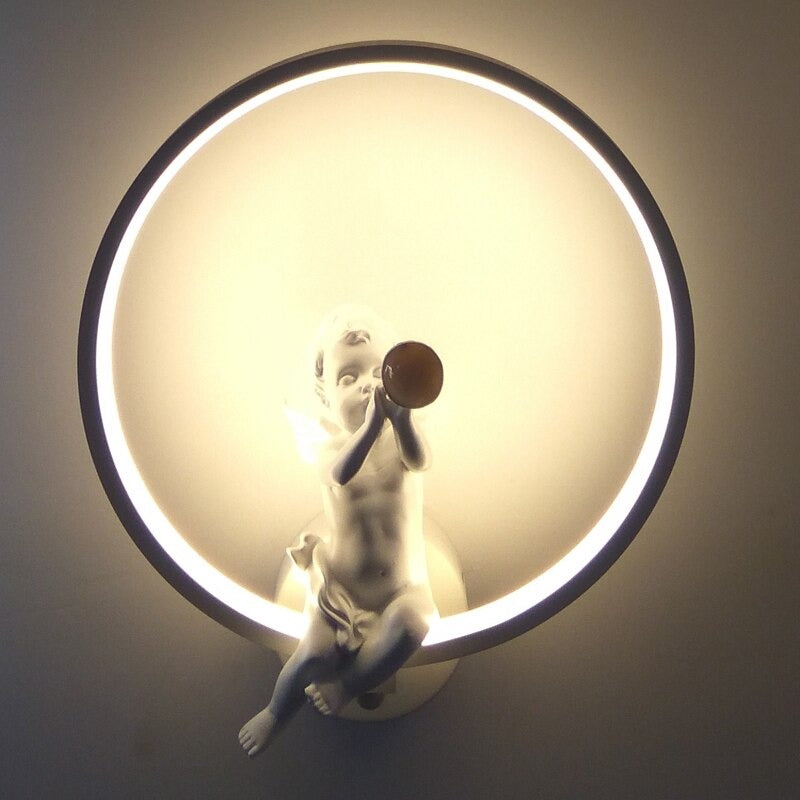 La Maison Applique "Applique murale cuisine design ange LED forme unique" représente un chérubin avec une trompette et une LED circulaire incandescente, projetant une douce lumière décorative pour un bel effet de halo.